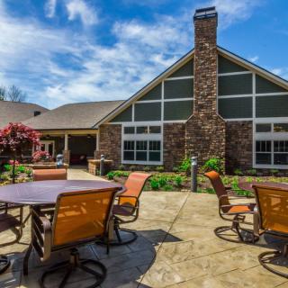 A spacious patio area with tables and chairs in front of a house with a chimney, set against a clear blue sky.