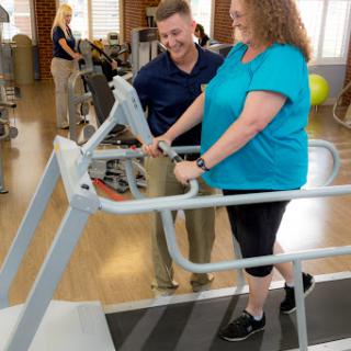 A healthcare professional assisting a patient during a physical therapy session on specialized exercise equipment.