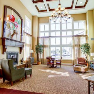 A spacious and well-lit living room featuring high ceilings, a chandelier, and large windows, complemented by comfortable furniture and a fireplace.