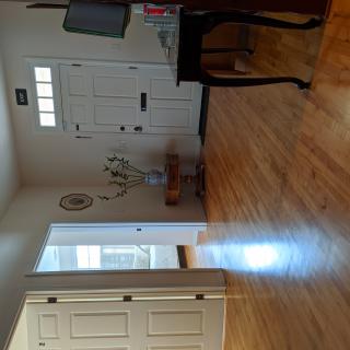 A bright entryway featuring a hardwood floor, a front door with windows, and furnishings such as a table and coat rack.