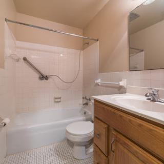 A compact bathroom featuring a bathtub with a shower, toilet, and wooden cabinetry.