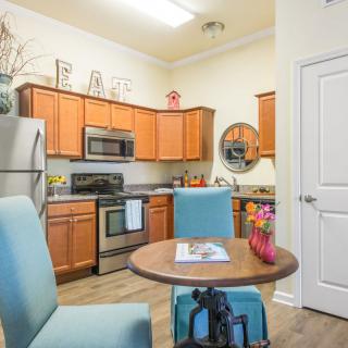 A cozy kitchen with wooden cabinets, stainless steel appliances, and a small dining table with blue chairs.