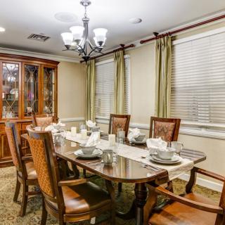 A classic dining room with a wooden table set for a meal, surrounded by chairs and illuminated by a chandelier.