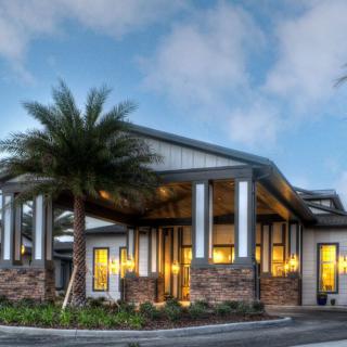 A modern house with sleek architecture surrounded by palm trees, illuminated in the evening.