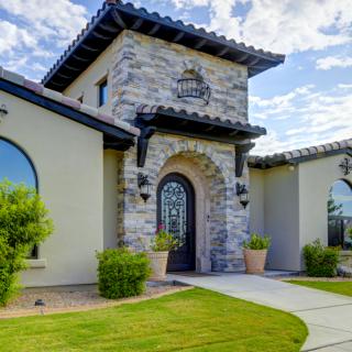 A stylish house with a stone facade and arched entrance surrounded by well-maintained landscaping.