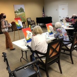 A group of seniors participating in a painting class, each working on their artwork at tables with easels.