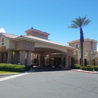 A modern hotel entrance with a palm tree and clear blue skies.