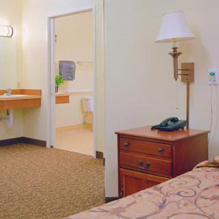 A cozy hotel room featuring a bed, nightstand with a lamp and telephone, and an adjoining bathroom.