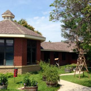 A cozy brick building surrounded by greenery, featuring a garden and pathway under a clear blue sky.