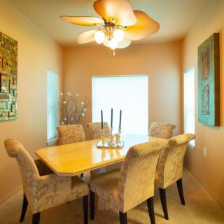 A cozy dining area with upholstered chairs around a wooden table, illuminated by a ceiling chandelier and adorned with wall art.