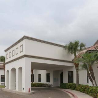 A building with an entrance canopy surrounded by palm trees under an overcast sky.