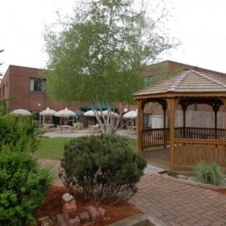 A quaint outdoor space featuring a gazebo, surrounded by lush greenery and patio seating with umbrellas.