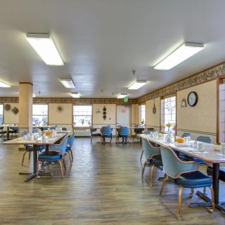 A spacious dining area with arranged tables and chairs, featuring natural lighting and a wooden floor.