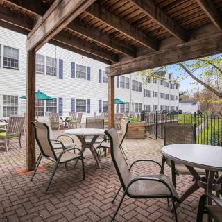 A covered outdoor patio area with tables and chairs, adjacent to a building with multiple windows.