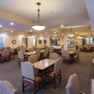 A spacious dining room with neatly arranged tables and chairs, featuring warm lighting and a carpeted floor.