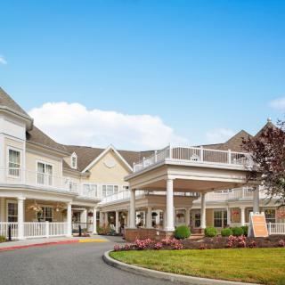 A large, multi-story residential building with a spacious entrance and landscaped surroundings under a clear blue sky.