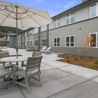 A modern outdoor patio area with tables, chairs, and an umbrella next to a building.