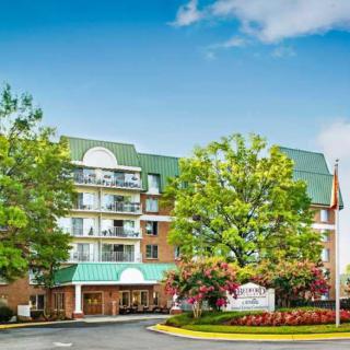 A multi-story hotel surrounded by trees and landscaping under a clear blue sky.