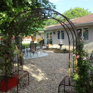 A beautiful garden with an archway leading to a patio area, featuring outdoor seating and surrounded by greenery.