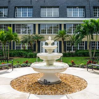 A beautifully landscaped courtyard featuring a central tiered fountain surrounded by palm trees and a well-maintained garden.