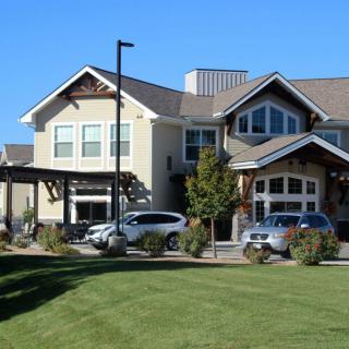 A modern residential building with parked cars and a grassy landscape.