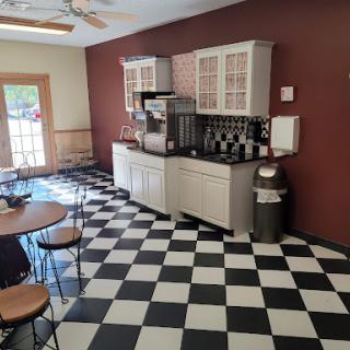 A modern kitchen with a checkered floor and coffee station, featuring simple dining furniture.
