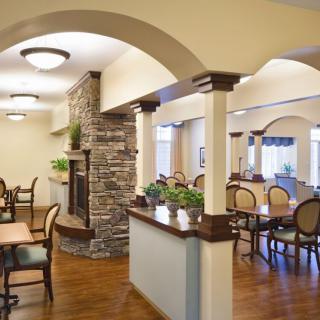 A cozy dining area with elegant arches and a stone fireplace, featuring stylish furniture and indoor plants.