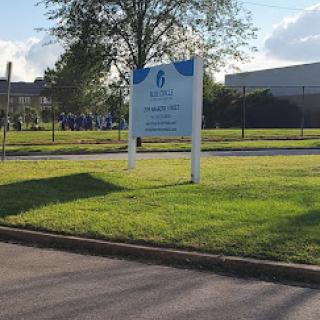 A sign outside a facility, surrounded by green grass and trees under a clear sky.