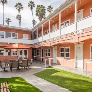 A charming courtyard with outdoor seating, surrounded by a two-story building and lush palm trees.