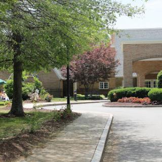 A peaceful scene featuring a pathway leading to a building surrounded by trees and landscaped gardens.