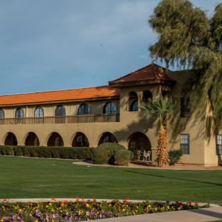 A two-story building with Spanish-style architecture surrounded by a well-maintained garden and palm trees.