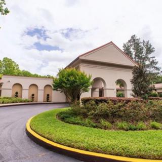 A scenic view of a building with arched entrances, surrounded by lush greenery and a curved driveway.