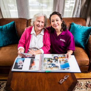 A joyful moment shared between an elderly woman and her caregiver as they look through a photo album filled with cherished memories.