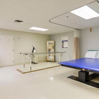 A clean, well-lit rehabilitation room equipped with a treatment table and parallel bars for physical therapy.