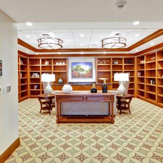 A well-appointed library featuring wooden bookshelves, a central desk, and decorative lighting.