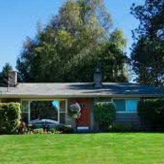A single-story house with a well-kept lawn and surrounding trees under a clear blue sky.