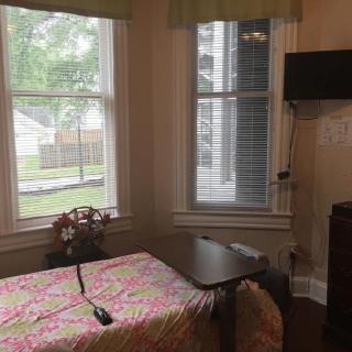 A cozy room with a single bed, a wall-mounted TV, and large windows offering natural light.