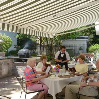A group of seniors enjoying an outdoor meal at a restaurant patio with a waiter taking orders.
