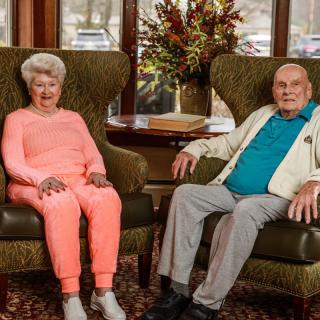 An elderly couple sitting on chairs in a cozy living room setting.
