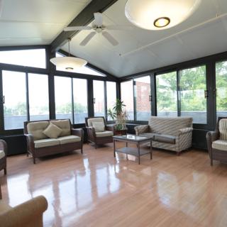 A spacious sunroom featuring modern furniture and large windows, complemented by a ceiling fan and indoor plants.