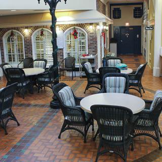 A cozy indoor seating area with wicker chairs and round tables on a brick floor, resembling a quaint cafe setting.