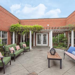 A cozy courtyard with green-cushioned seating, a wooden bench, and a pergola adorned with plants.