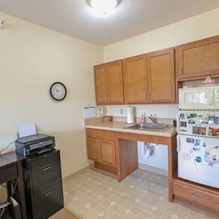 A small kitchen with wooden cabinets, a fridge, microwave, and a clock on the wall.