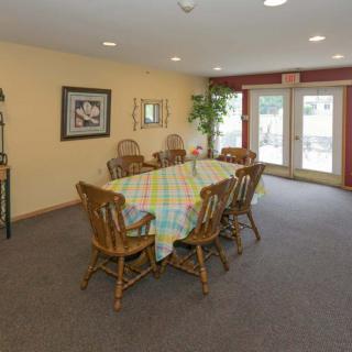 A cozy dining room with a wooden table set and chairs, decorated with a colorful tablecloth and surrounded by artwork and plants.