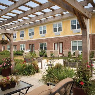 A beautifully landscaped garden patio with outdoor seating and a pergola, adjacent to a multi-story building.