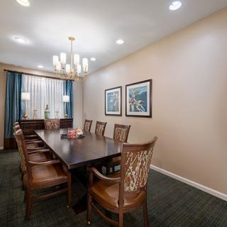 A well-lit dining room with a long wooden table, several chairs, and two framed artworks on the wall.