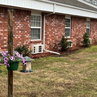 A brick house with several windows, a lawn, and a flower pot of purple flowers in the yard.