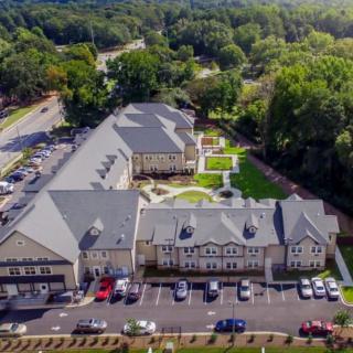 Aerial view of a large building complex surrounded by trees, with a parking lot in the front.