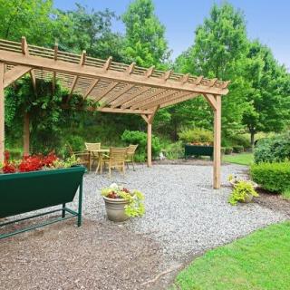 A serene garden with a wooden pergola and outdoor seating area surrounded by lush greenery.