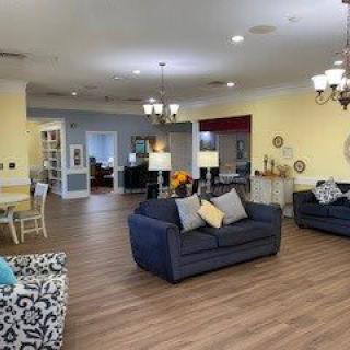A cozy and well-lit living room featuring comfortable sofas, elegant chandeliers, and a wooden floor.